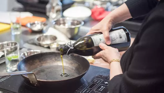 Des mains qui versent de l'huile d'une bouteille dans une poêle à frire de métal sur une cuisinière à un brûleur.