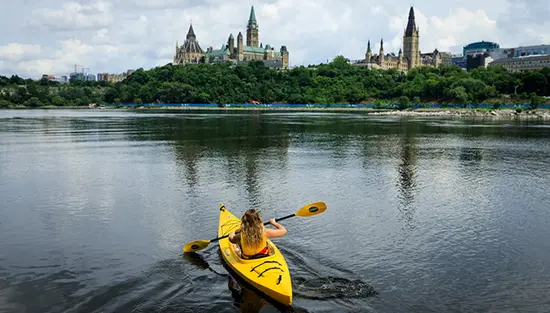 Une femme dans un kayak jaune pagayant vers la Colline du Parlement à Ottawa.