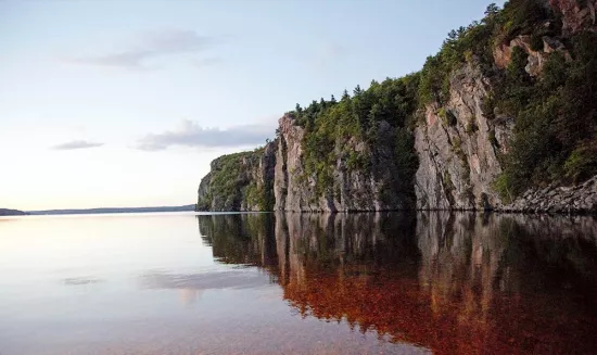 Le reflet d’un énorme rocher escarpé sur des eaux calmes.